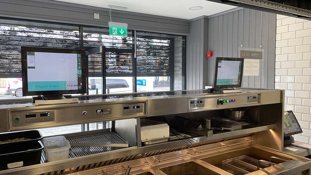 Two ICRTouch TouchKitchen digital kitchen display systems in use at a fish & chip shop