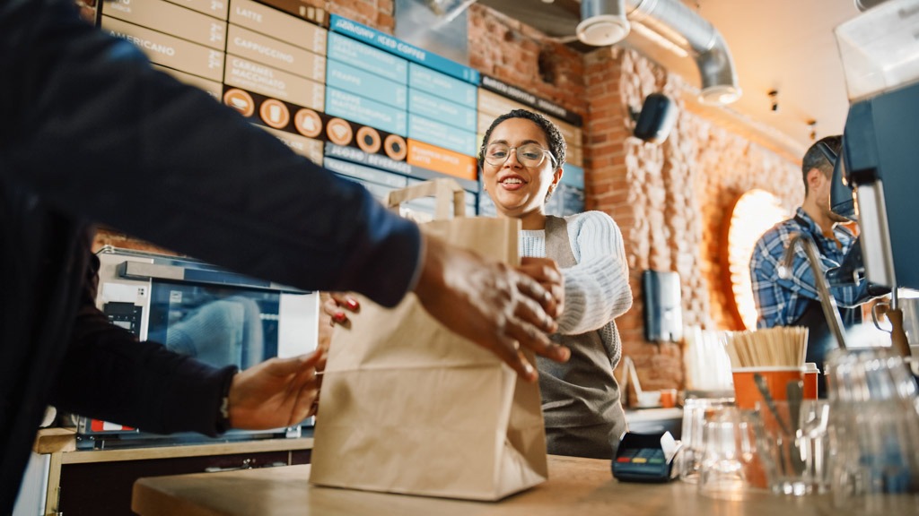 Barista passing a customer their order in a brown paper bag at a cafe